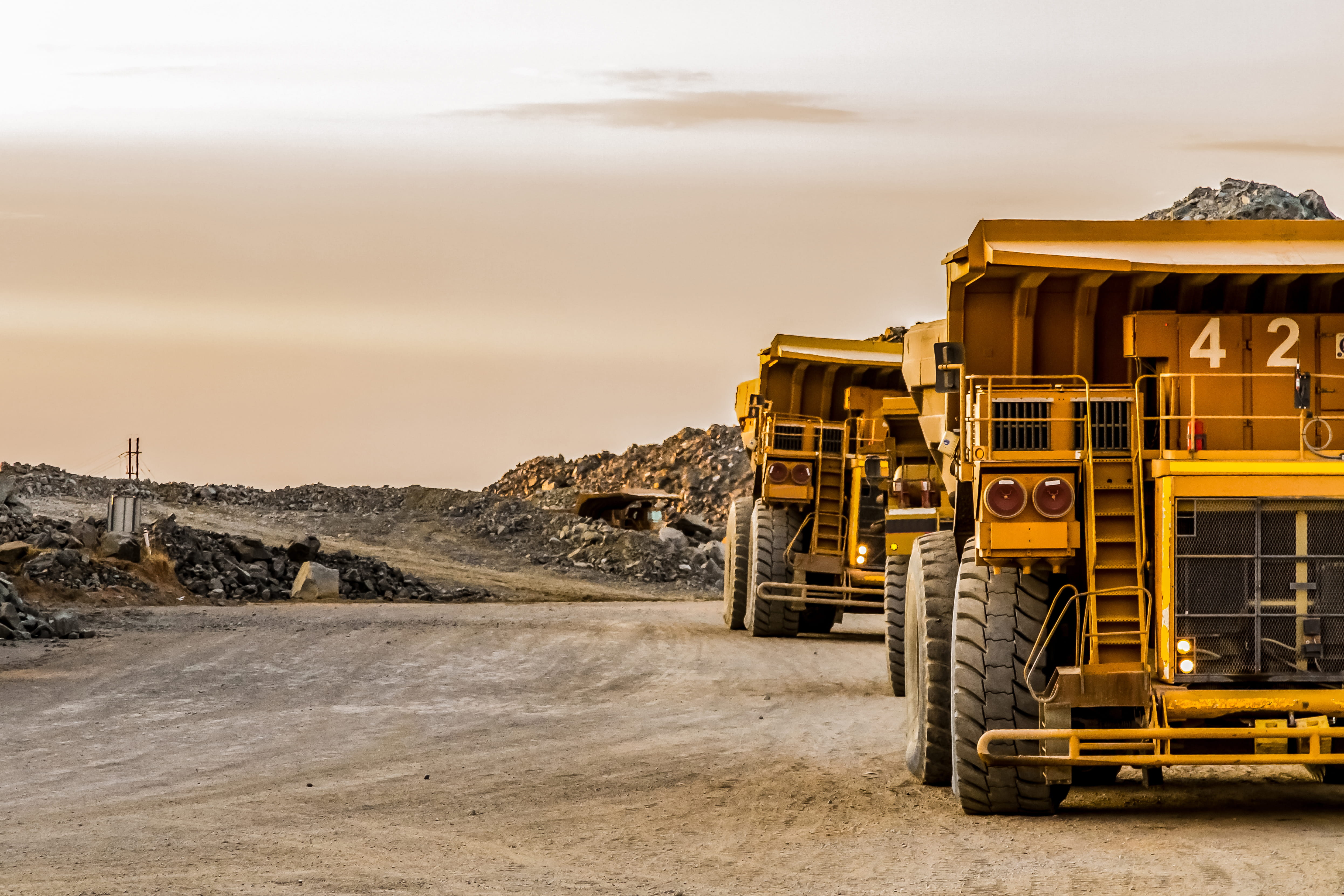 2 yellow lorries lined up driving towards the same direction from a construction site