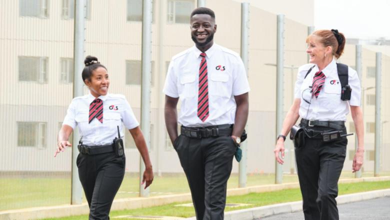 Three smiling G4S custodial officers in white shirts and ties walking together outside a secure facility.