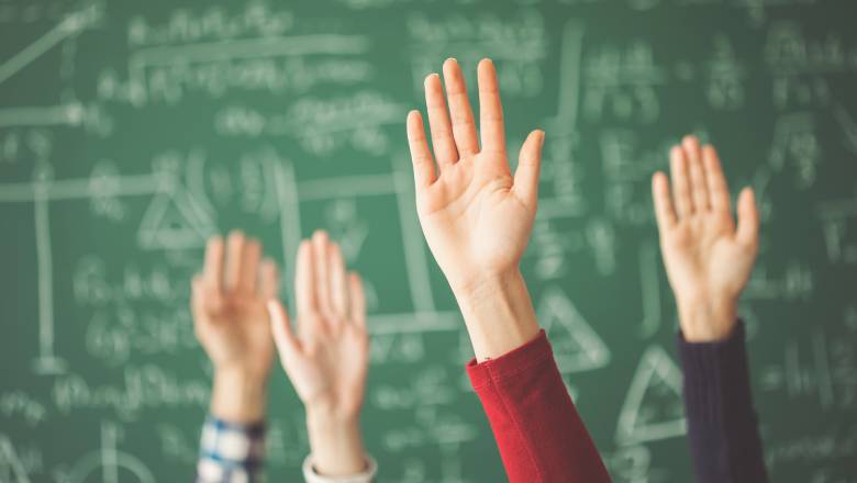Four hands in the air in front of a blackboard