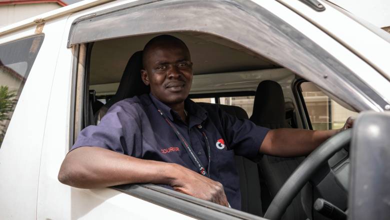 A G4S courier sat in the drivers seat of his G4S delivery vehicle looking down the lens of the camera