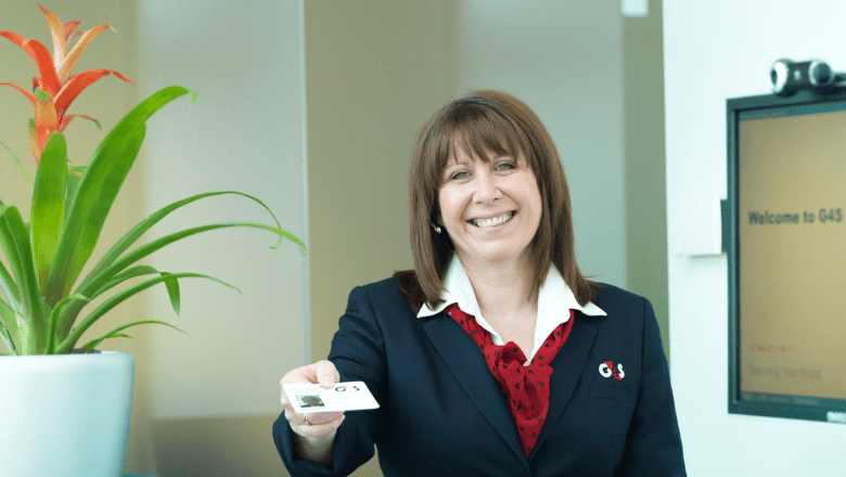 G4S Facilities Management receptionist smiling and handing a visitor badge to a guest