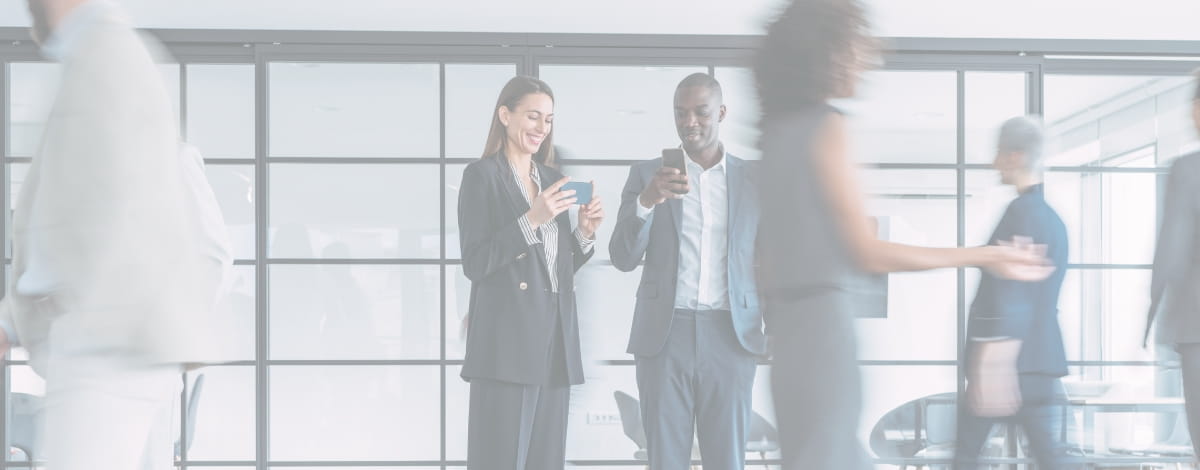 Blurred office setting with two professionals in suits looking at their smartphones.
