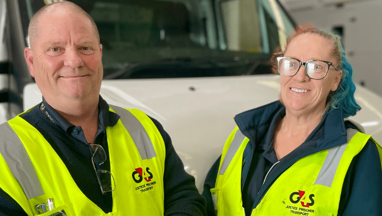 2 prisoner transport officers in neon yellow G4S vests looking at the camera and smiling, standing in front of a truck