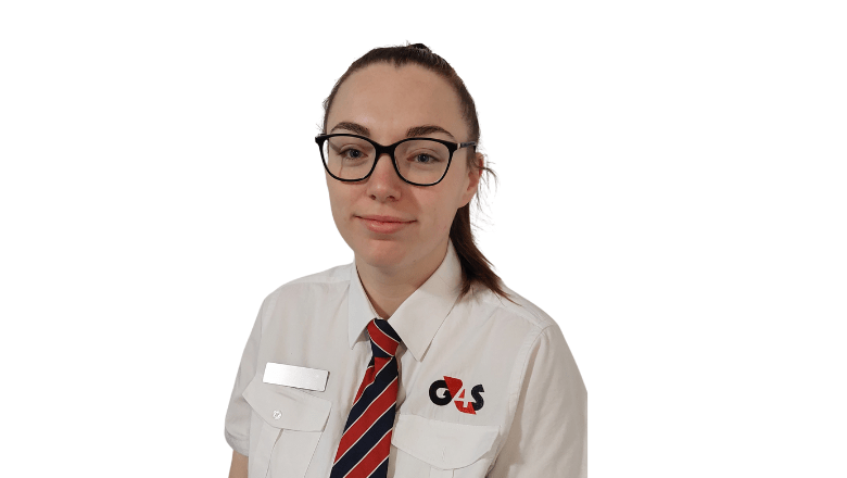 A female Correctional Officer in black glasses and a white polo shirt looks at the camera smiling