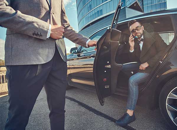 Mand på vej ud af bil. Livvagt holder døren.