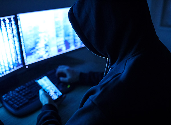 Mand med hætte der hacker telefon og computer