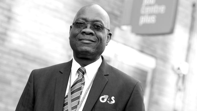 Male wearing G4S suit jacket standing outside in front of brick wall