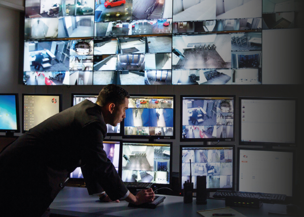Male G4S staff member monitoring security cameras on premises via large computer screens