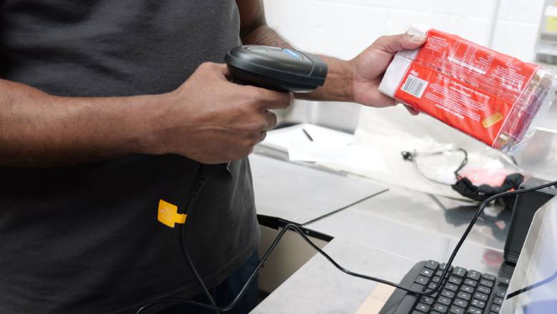 A person is scanning a red packaged item with a handheld barcode scanner at a checkout counter