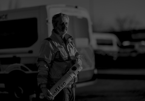 Patient Transport Services crew member holding an oxygen cylinder, with an ambulance in background.