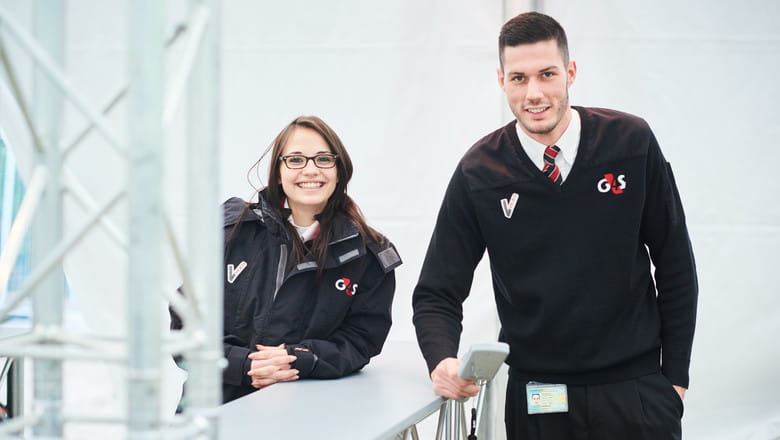 Female and male staff members looking and smiling at camera wearing G4S uniform in a prison setting