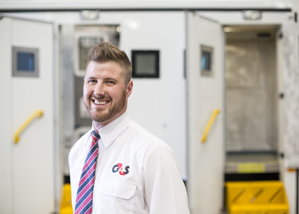 G4S Employee wearing white shirt in front of prisoner transport bus.