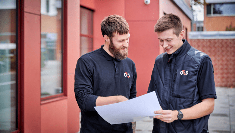 Tehniskie darbinieki G4S formas tērpos skatās dokumentu, kas abiem rokās. 