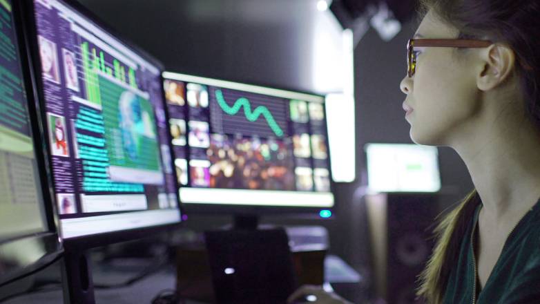 A female security specialist reviewing data on two computer screens in a GSOC (stock image)